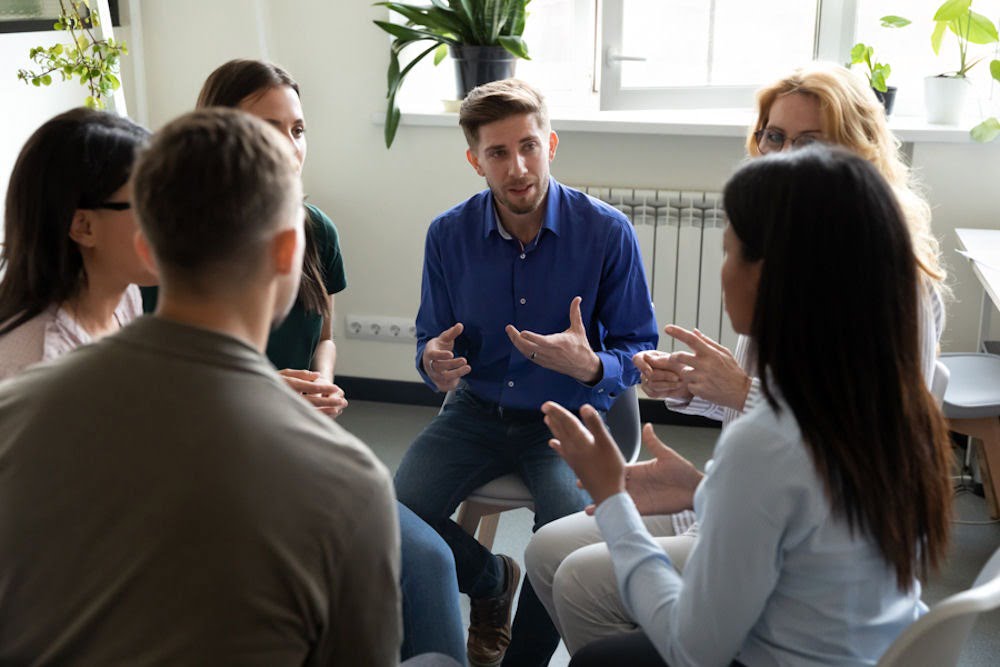 a man wearing blue shirt talking to a group of patients