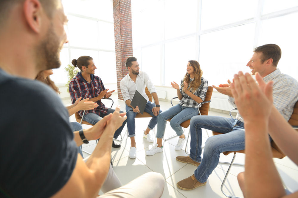 group therapy session with everyone in chairs and clapping in congratulations