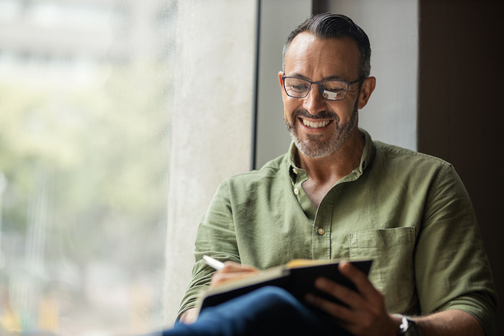 Man writing in journal during recovery by the windowsill