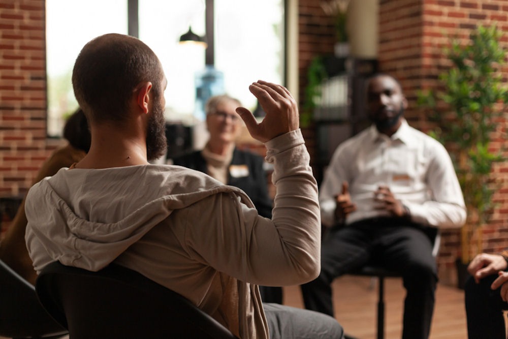 a man raising hand in group therapy