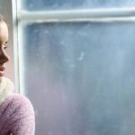 Young woman showing signs of high functioning anxiety while quietly reflecting by a window